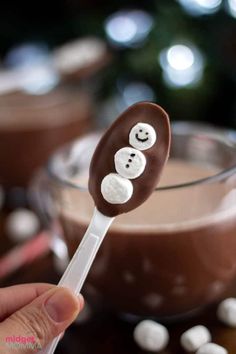 a person holding a spoon with chocolate covered marshmallows in the shape of faces