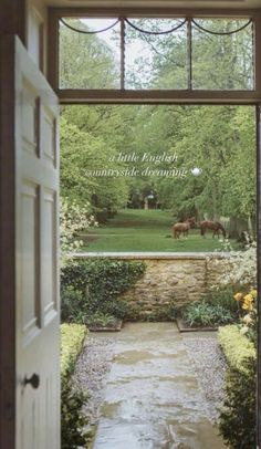 an open door leading to a lush green yard with horses in the distance and flowers on either side