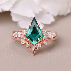 an emerald colored stone surrounded by white diamonds on top of a rose - shaped ring