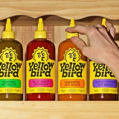 three bottles of yellow bird hot sauce in a wooden box with a hand reaching for one bottle