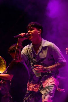 a man with tattoos on his arm singing into a microphone in front of purple lights