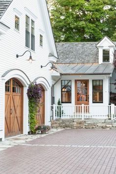 a white house with two brown doors and brick walkway leading up to the front door