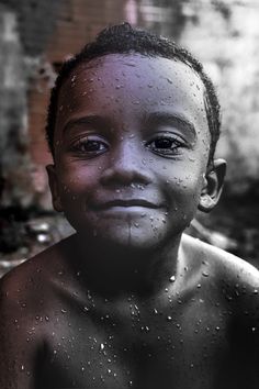 a black and white photo of a young boy with water droplets on his face, smiling at the camera