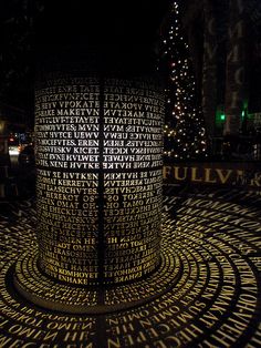 the words are written in many languages on this circular display with lights and christmas trees behind it