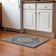 a kitchen with white cabinets and wood floors, including a blue rug on the floor