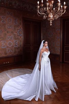 a woman in a wedding dress standing on a wooden floor with a chandelier