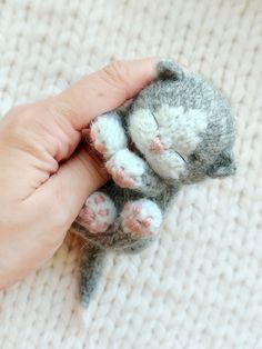 a hand is holding a small gray and white kitten toy with pink paws on it's belly