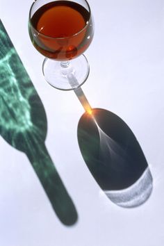 a glass of wine sitting on top of a table next to a shadow of a spoon