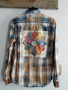 a plaid shirt hanging on a wooden hanger next to a wall with a flower embroidered on it