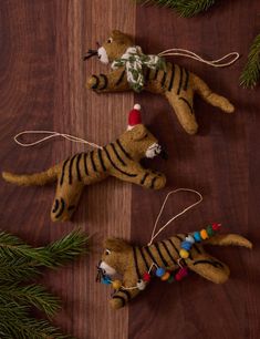 three stuffed animals hanging from christmas decorations on a wooden table with pine branches and needles