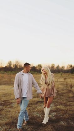 a man and woman holding hands walking through an open field