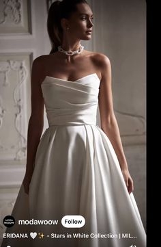 a woman in a white wedding dress with pearls on her neck and shoulders, standing next to a wall