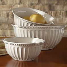 three white bowls with fruit in them sitting on a table next to a brick wall