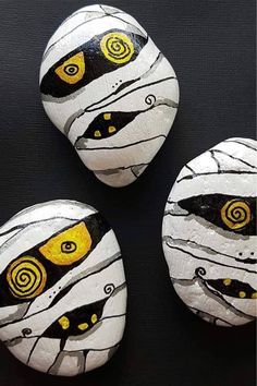 three painted rocks sitting on top of a black surface with yellow and white circles in the middle