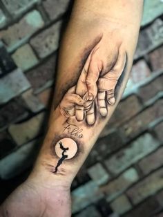 two hands holding each other with the moon and key tattoo on their forearms, in front of a brick wall