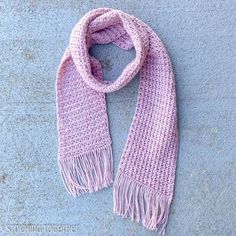 a pink knitted scarf laying on top of a cement floor next to a blue wall