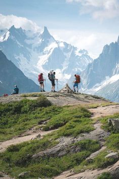 three people with backpacks are standing on top of a hill looking at the mountains