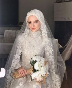 a woman in a wedding dress holding a bouquet and wearing a veil with flowers on it