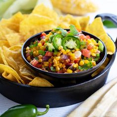 a black bowl filled with corn salsa and tortilla chips