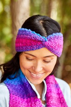 a woman wearing a purple and blue knitted headband smiles at her cell phone