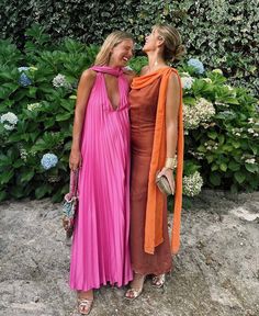 two women standing next to each other in front of bushes