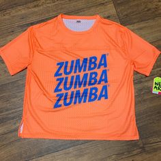 an orange shirt with the word zumba on it is laying on a wooden floor