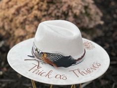 "The Lainey Wilson Concert Wide Brimmed Cowgirl Hat - Thick as Thieves design is perfect for attending that upcoming Lainey concert... Or just displaying your fan crush!   Colors: Cream Sand (Light Tan) Cognac (Dark Tan) Each hat displays the \"Thick as Thieves\" lettering and a floral arrangement burned-by-hand around the hat brim, as well as, a Lainey Wilson concert ticket stub. Flowers are just my creative arrangements, but feel free to let me know if you have a specific flower that you would Lainey Wilson Hats, Custom Cowboy Hats, Concert Attire, Hat Display, Felt Cowboy Hats, Dark Tan, Concert Tickets, Cowgirl Hats, Wide Brimmed