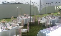 tables and chairs are set up in the grass for a formal function with white tablecloths and pink napkins