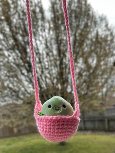 a green stuffed animal in a pink crocheted hammock