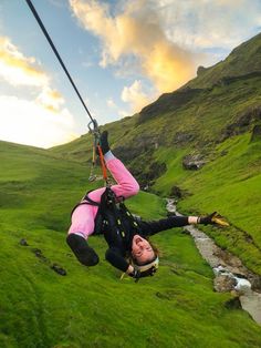 a woman hanging from a rope in the middle of a grassy field with a river running through it