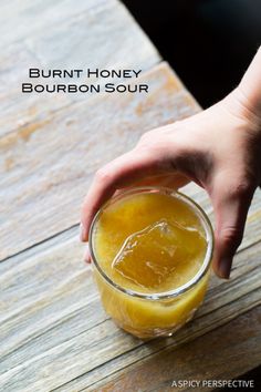 a person is holding a jar of honey bourbon sour on a wooden table with text overlay that reads burnt honey bourbon sour