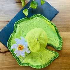 a crocheted green hat with a flower on it sitting on a wooden table