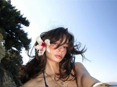 a woman with flowers in her hair standing on the beach looking off into the distance