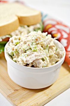 a white bowl filled with chicken salad on top of a cutting board next to a sandwich