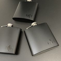 three black flasks with initials on them