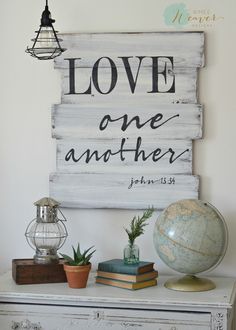 a wooden sign that says love one another on top of a table with books and plants