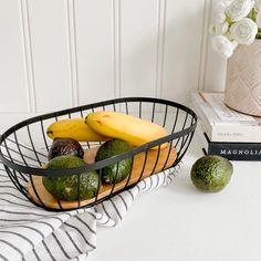 a basket filled with fruit sitting on top of a table next to a book and vase