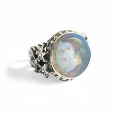 The subject of this ring is the moon and stars expressed in iridescent aurora satin glass. Light moves through the glass every way you position your hand, opalescent and glowing in soft hues of blue, purple, aqua, peach and lavender. It is surrounded by an aurora crystal border with three carved stars on both sides which join it to the ring shank, a tapering, comfortable pierced band that may be adjusted to fit sizes 6 through 9. Choice of metal finish in burnished bronze or antique silver. Made Mystical Silver Opal Ring, Silver Moon-shaped Celestial Moonstone Ring, Silver Celestial Moonstone Ring, Celestial Silver Moonstone Ring, Celestial Crystal Ring With Moon Phase, Celestial Silver Moonstone Ring With Sun And Moon Design, Silver Moonstone Ring With Sun And Moon Design, Celestial Moon Phase Crystal Ring, Celestial Style Opal Ring