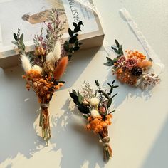 three dried flowers sitting on top of a table next to an open box with a book in the background