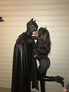 two people dressed up as batman and catwoman kissing in front of a garage door