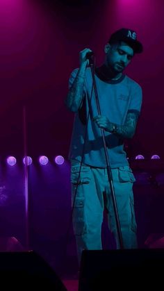 a man holding a microphone while standing in front of purple and blue lights at a concert