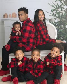 a family wearing matching red and black flannel outfits sitting on a white bench