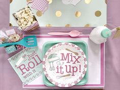 a pink and green table setting with gold confetti, paper plates, spoons and utensils