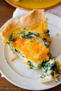 a slice of quiche with spinach and cheese on a plate next to a fork