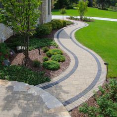 a walkway in front of a house with trees and bushes on both sides, surrounded by landscaping