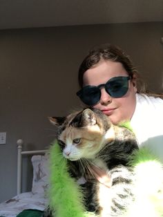 a woman wearing sunglasses and holding a cat in her arms, while sitting on a bed