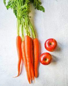 carrots, apples and parsley laid out on a white counter top with the tops still attached