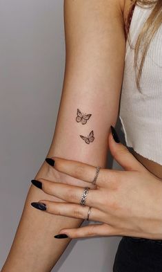 two women with matching tattoos on their arms holding each other's hands and one has a butterfly tattoo on her left arm