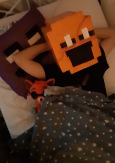 a person laying in bed with an orange block on their head and a stuffed animal