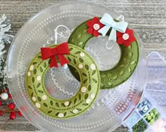 two green christmas wreaths sitting on top of a glass plate